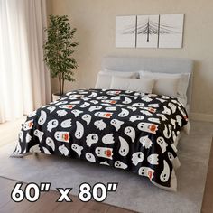 a bed with black and white ghost bedspread on top of it next to a potted plant