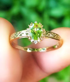 a close up of a person's hand holding a ring with a green stone