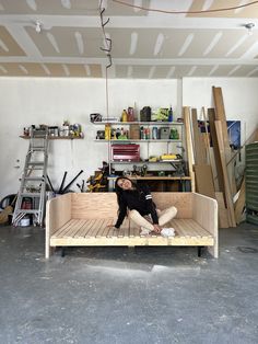 a woman sitting on top of a wooden bench in a room filled with shelves and ladders