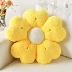 a yellow flower shaped pillow sitting on top of a white couch next to a vase with flowers