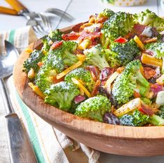 a wooden bowl filled with broccoli salad on top of a table next to utensils