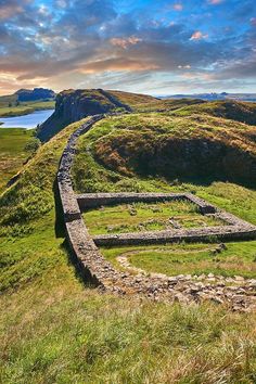 an old stone wall on the side of a grassy hill with water in the background