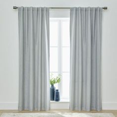 an open window with curtains and rugs in front of it, next to a potted plant