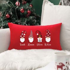 a red pillow sitting on top of a white couch next to a christmas tree with santa hats