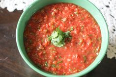 a green bowl filled with red sauce and garnish on top of a wooden table