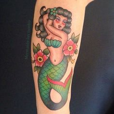 a woman's tattoo with a mermaid on her arm and flowers around her ankles