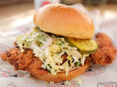 a fried chicken sandwich with coleslaw and pickle on it sitting on top of a paper wrapper