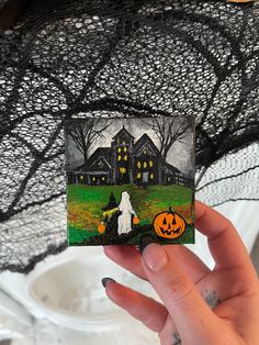 a hand holding up a halloween card with a ghost and pumpkin in front of a house