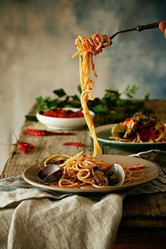 spaghetti being lifted from a plate by tongs on a wooden table with other dishes in the background