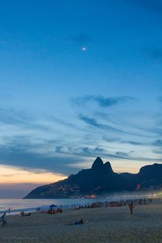 people are on the beach at dusk with mountains in the background