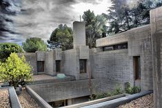 an abandoned concrete building with trees in the back ground and clouds in the sky above