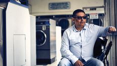 a man sitting on the side of a washer machine in a laundroom