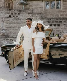 a man and woman standing next to a car with the door open, dressed in white