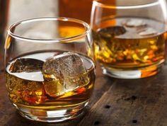 two glasses filled with ice sitting on top of a wooden table next to each other