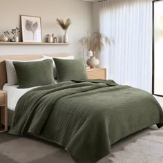 a bed in a bedroom with a green comforter and pillows on top of it