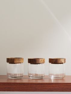 three glass jars with wooden lids sit on a shelf