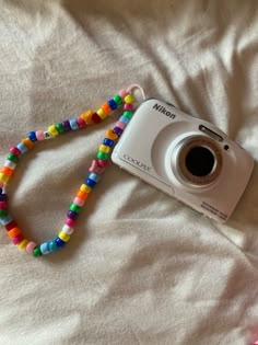 a camera with a colorful beaded lanyard attached to it's body on a bed