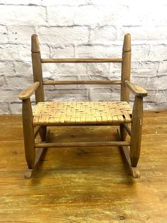 a wooden rocking chair sitting on top of a hard wood floor next to a white brick wall