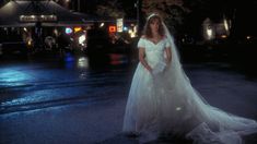 a woman in a white wedding dress standing on the street at night with her veil pulled back