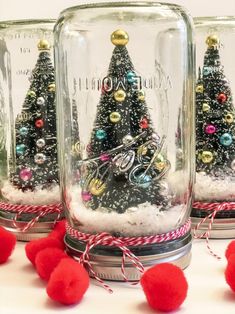 three glass jars with christmas trees in them and some red pom - poms