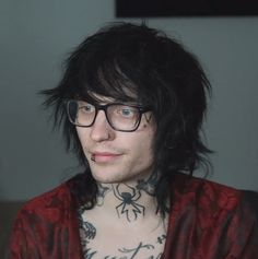 a man with tattoos on his chest wearing glasses and a red jacket is looking at the camera