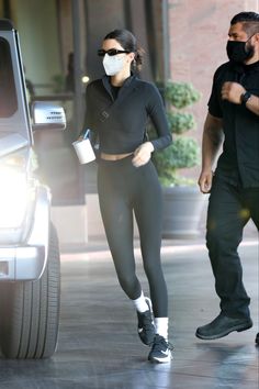 a woman in black sports bra and leggings is walking towards a car while wearing a face mask