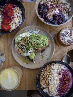 an overhead view of several bowls of food on a wooden table with utensils