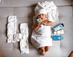 a baby laying on top of a couch next to items