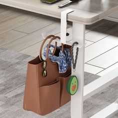 a purse hanging from the side of a white table next to a laptop on a desk