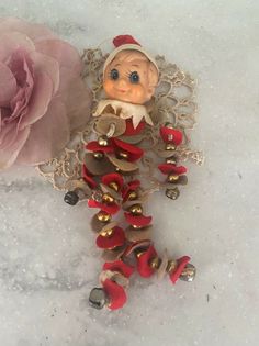 a small doll is sitting next to a flower on the snow with beads and bells around it