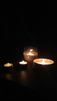 three lit candles sitting on top of a wooden table next to a glass bowl filled with water