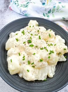 a black plate topped with dumplings covered in sauce and green onions next to a napkin