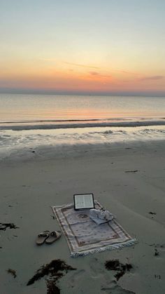 an open book sitting on top of a sandy beach next to the ocean at sunset