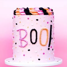 a white cake with pink frosting and black letters on the top is decorated with sprinkles