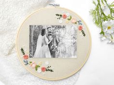 an embroidered photo frame with flowers around it and a bride and groom in the background