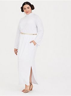 a woman wearing a white dress with gold belt and high heeled sandals standing in front of a white background