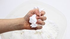 a hand is holding some white powder in front of a bowl full of sugar and water