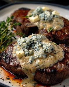 two steaks with blue cheese sauce on top and green herbs in the middle, sitting on a white plate