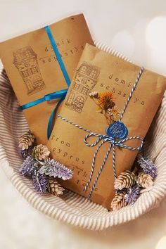 two wrapped gifts in a basket with blue ribbon and pine cones on the bottom, tied with twine