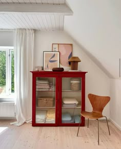 a red cabinet sitting on top of a hard wood floor next to a wooden chair