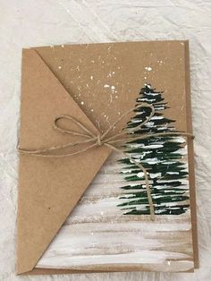 a card with a christmas tree painted on it and tied up to a brown envelope