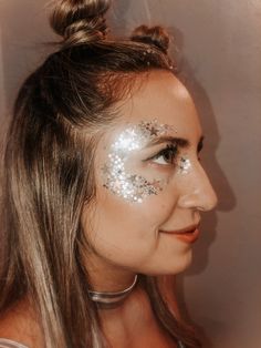 a woman with silver glitter on her face and hair in a pony tail style bun