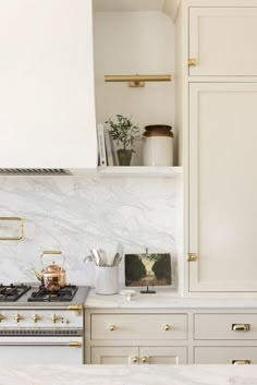 a kitchen with white cabinets and marble counter tops, gold pulls on the oven hood