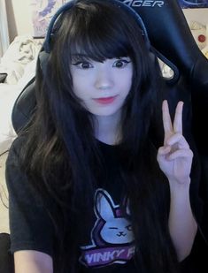 a girl with long black hair wearing headphones and making the peace sign in front of her face