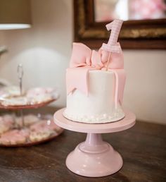 a pink cake with a bow on top sits on a table next to other desserts