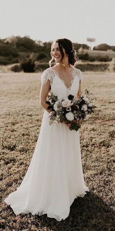 a woman in a wedding dress standing in a field holding a bouquet and looking at the camera