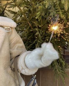 a person holding a sparkler in their hand near a christmas tree that has been decorated with lights