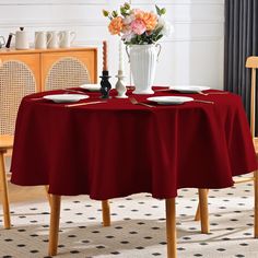 a dining room table with red cloths and white plates on it, in front of a vase filled with flowers