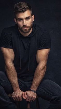 a man sitting on top of a stool with his hands in his pockets and looking at the camera