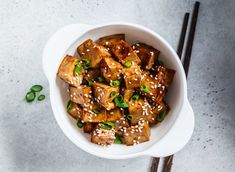 tofu with sesame seeds and green onions in a white bowl next to chopsticks